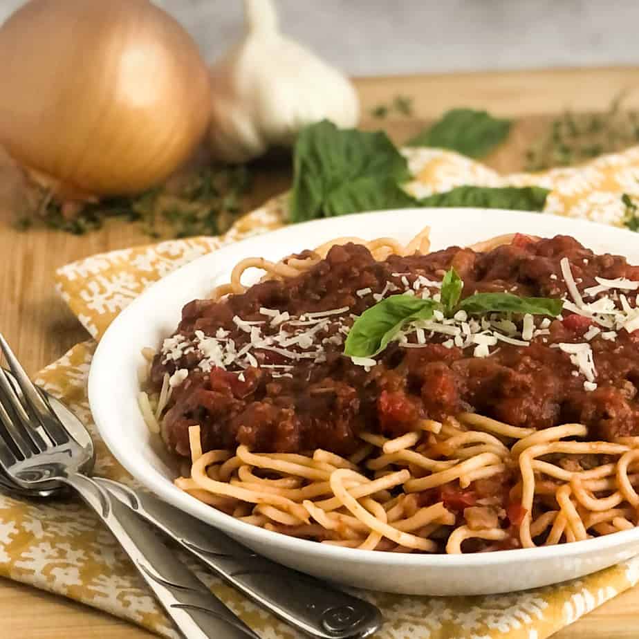 Ragu Meat Sauce over spaghetti in a white bowl garnished with fresh basil and parmesan.