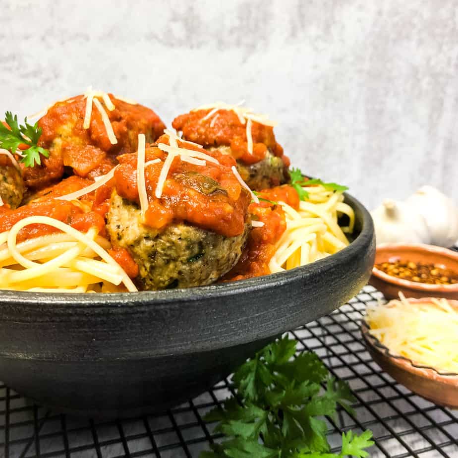 Close up shot of turkey meatballs nestled into spaghetti, topped with marinara sauce, in a black bowl.