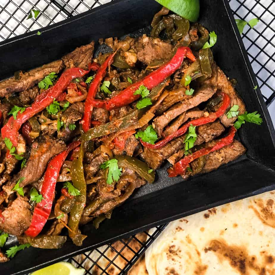 Steak Fajitas on a black platter garnished with cilantro and lime wedges.