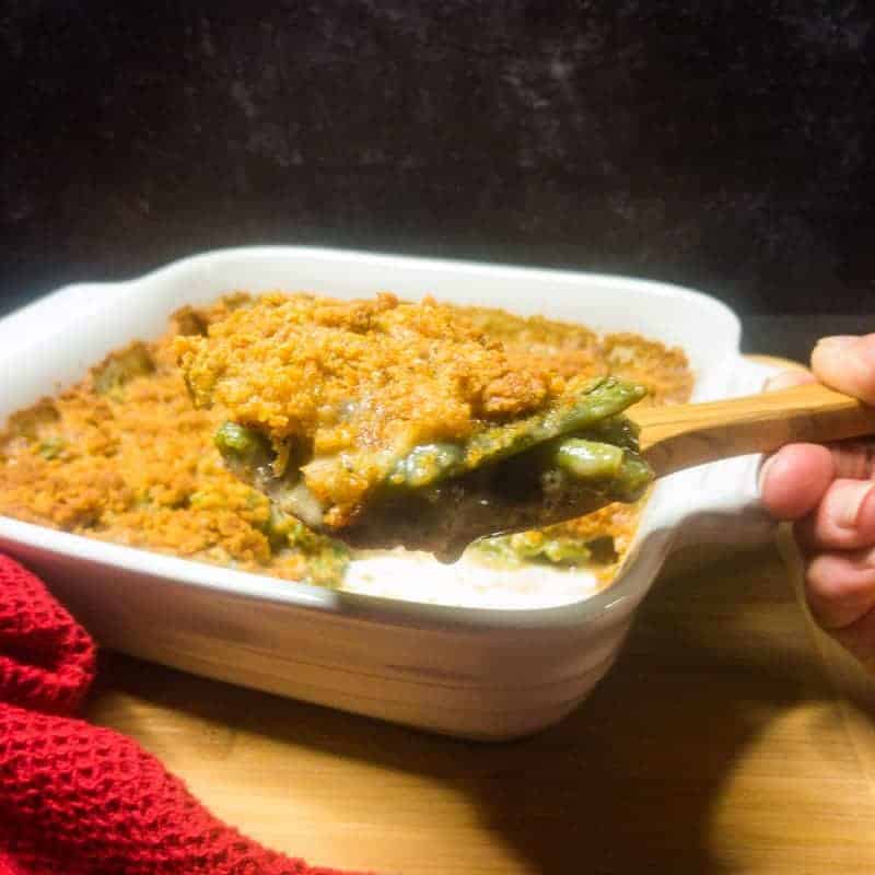 Green Bean Casserole in a white dish on top of a brown cutting board with a spoon holding a scoop.