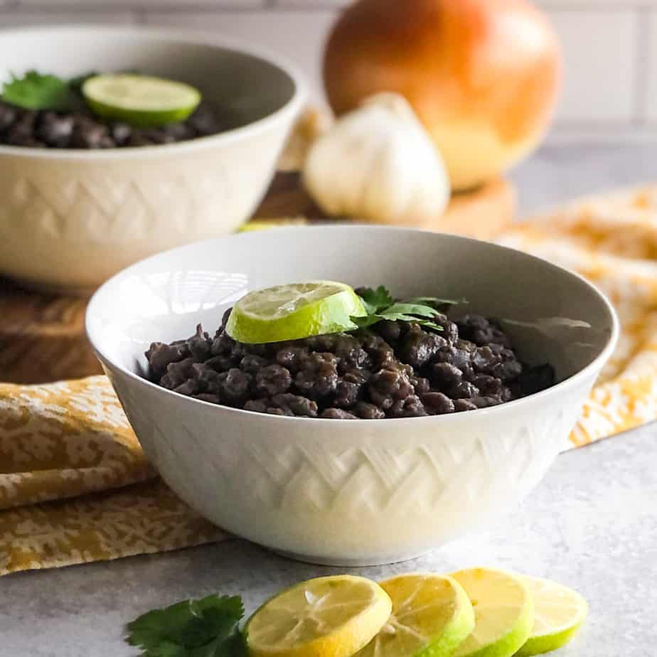 Close up of Mexican Black Beans in a white bowl garnished with cilantro and lime wheels.