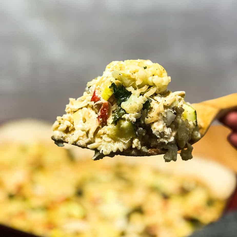 Wooden spatula holding a scoop of cheesy chicken and rice casserole.