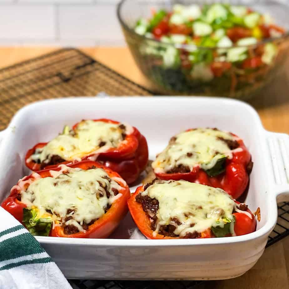 Cooked peppers in casserole dish with salad in background.