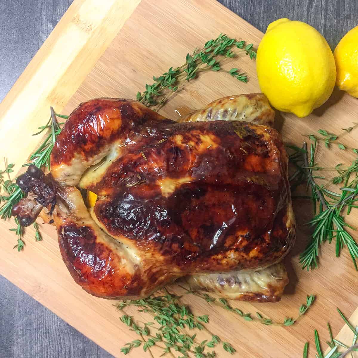 Roasted Chicken on a wood cutting board garnished with fresh herbs and lemons.