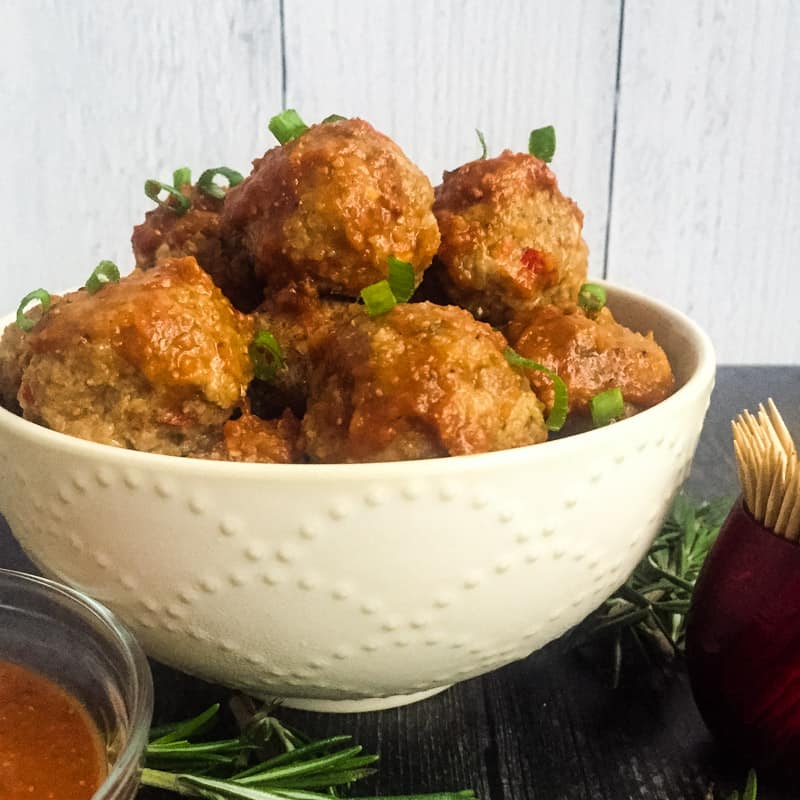 Side view of BBQ Turkey Meatballs in a white bowl with chopped chive garnish.
