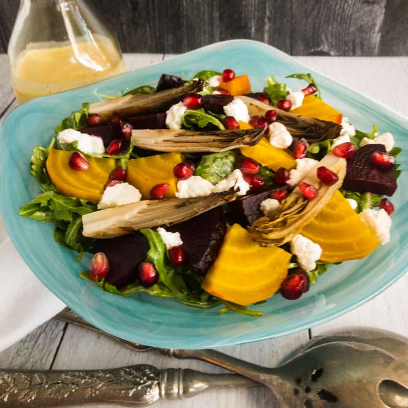 Roasted Beet and Endive Salad in a blue bowl with a dressing bottle in the back and silver salad spoons in front.