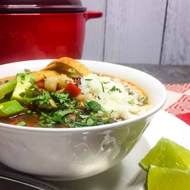 Vegetarian Tortilla Soup in a white bowl garnished with cheese, tortilla strips, avocado, cilantro, and lime.