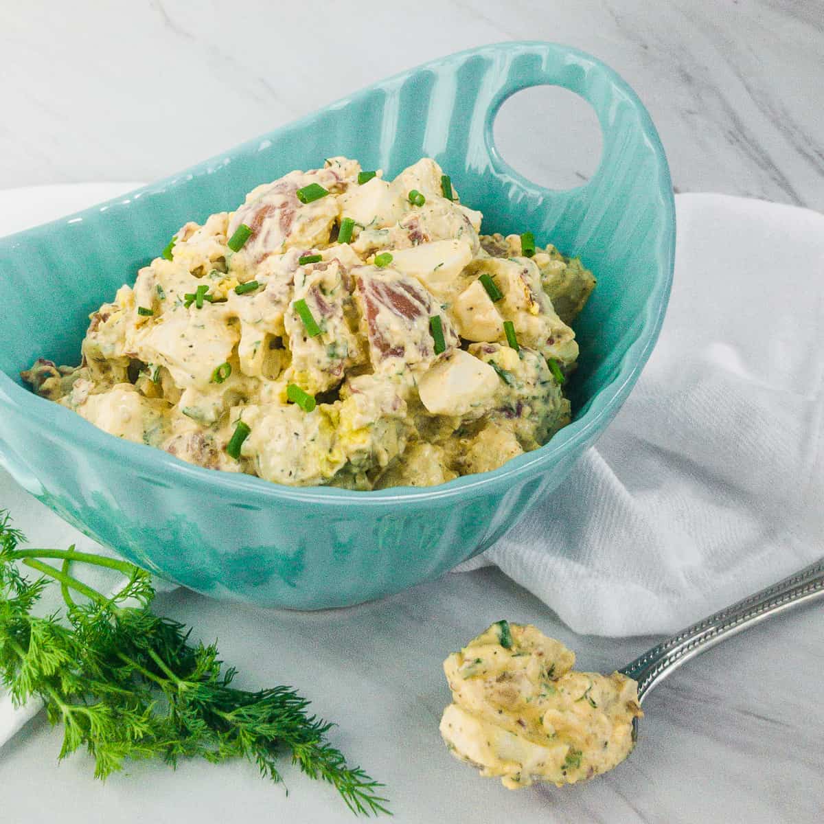 Potato Salad in a blue bowl with a spoon of potato salad in foreground.