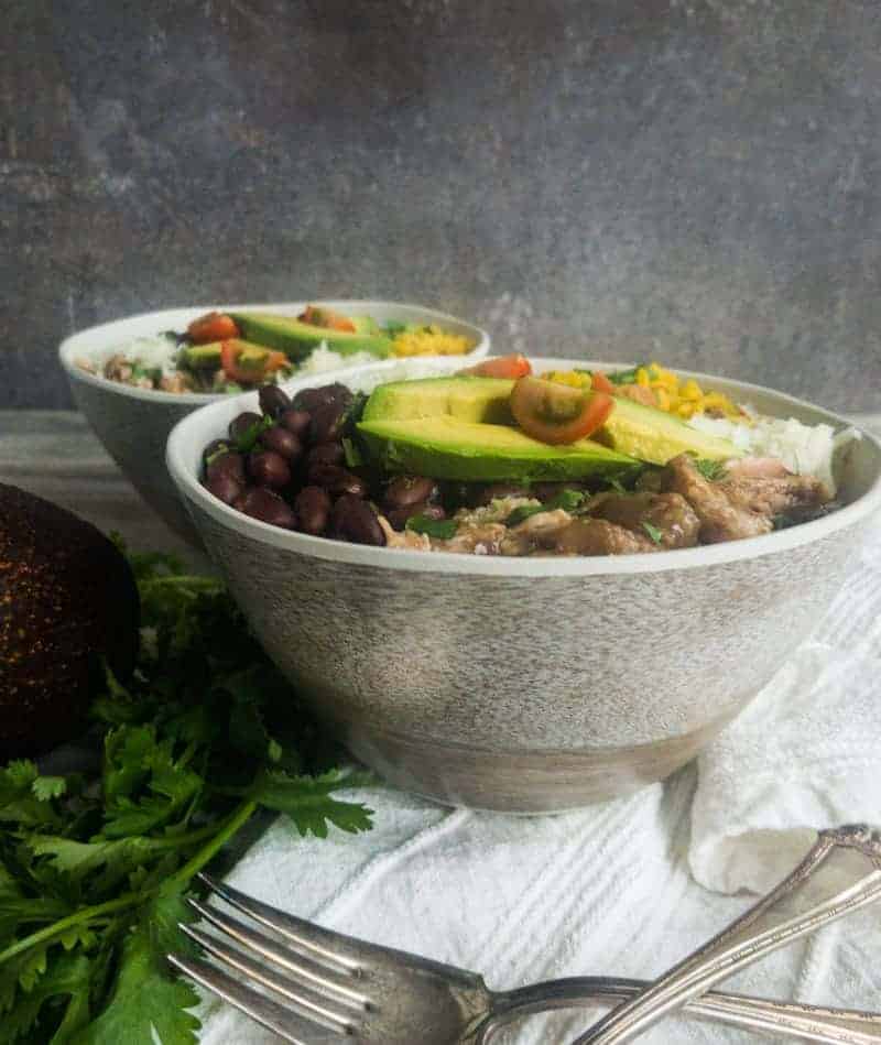 Close up shot of two pork carnitas bowls with black beans, yellow rice, manchego cheese, avocado, and tomato.