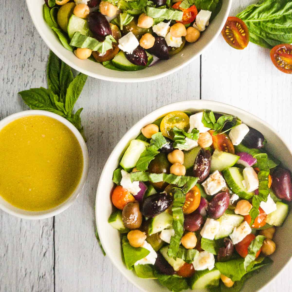 Two bowls of salad with a small bowl of dressing next to them.