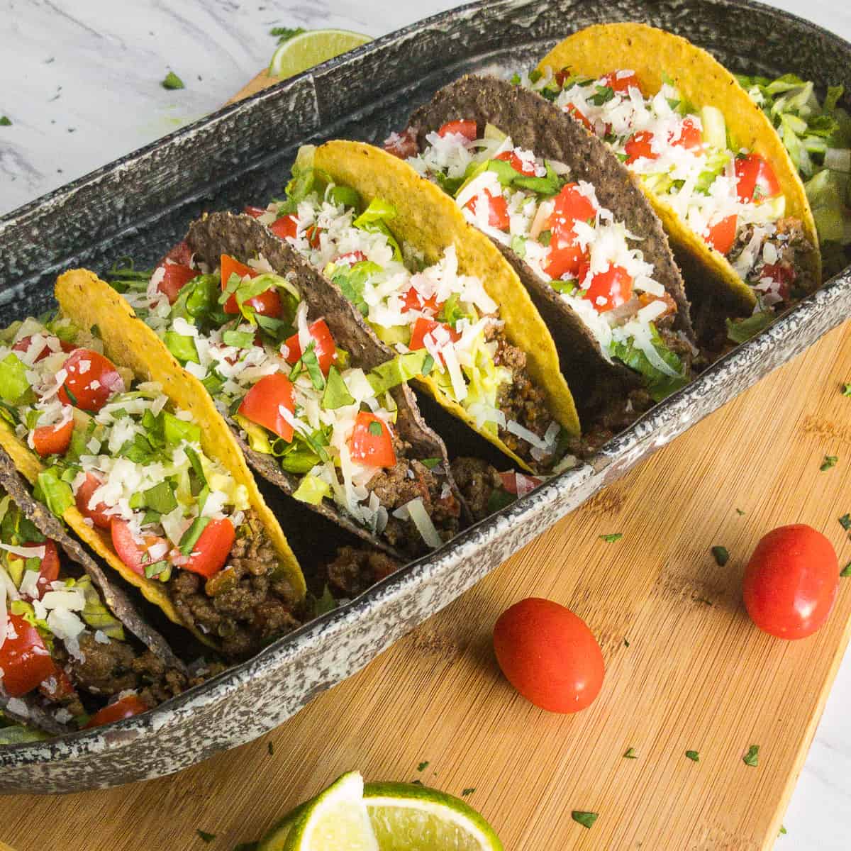 Hard shell tacos on a platter garnished with lettuce, tomato, and cheese.