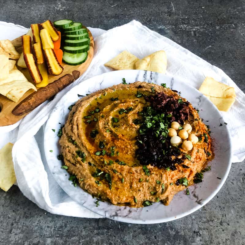 Close of Mediterranean Hummus on a faux marble plate with vegetable slices and pita chips in the background.