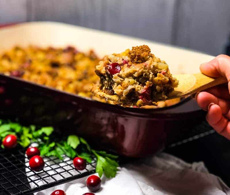 A serving of Gluten-free Vegetarian Stuffing on a wooden spatula with casserole in the background.