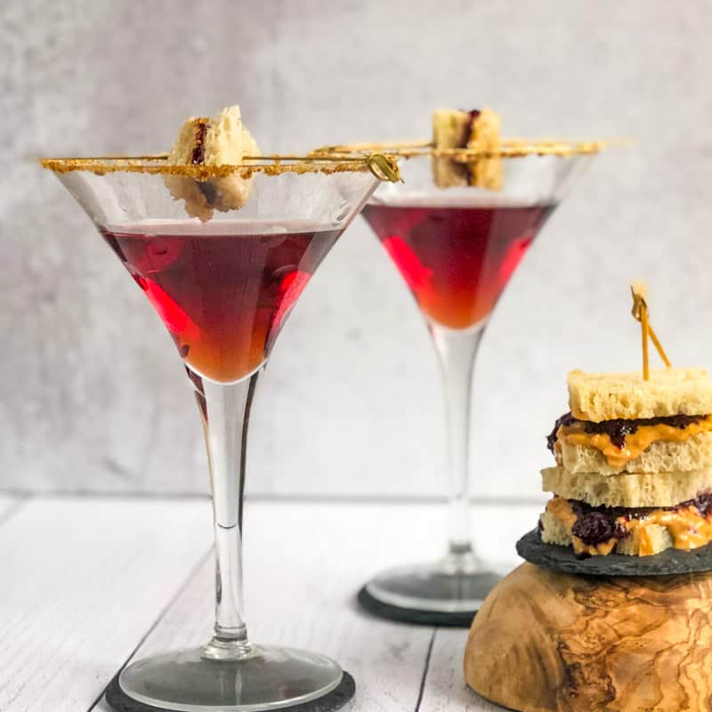 Peanut Butter and Jelly Martini with a small stack of peanut butter and jelly sandwiches to the side.