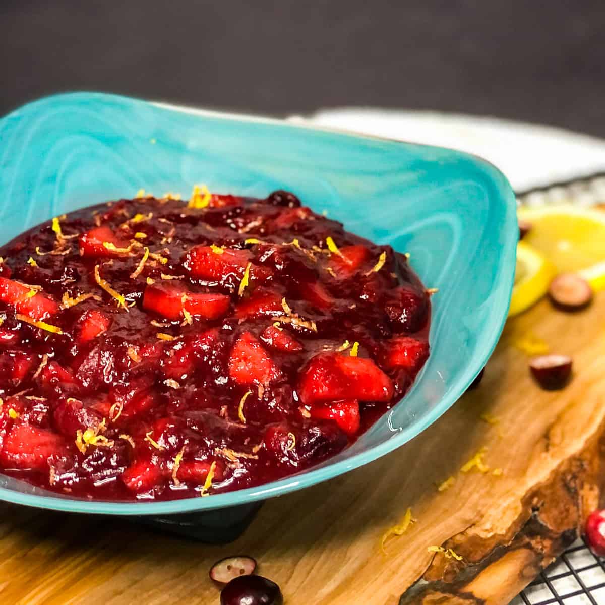 Close up of Cranberry Applesauce in a blue bowl on a wood platter.