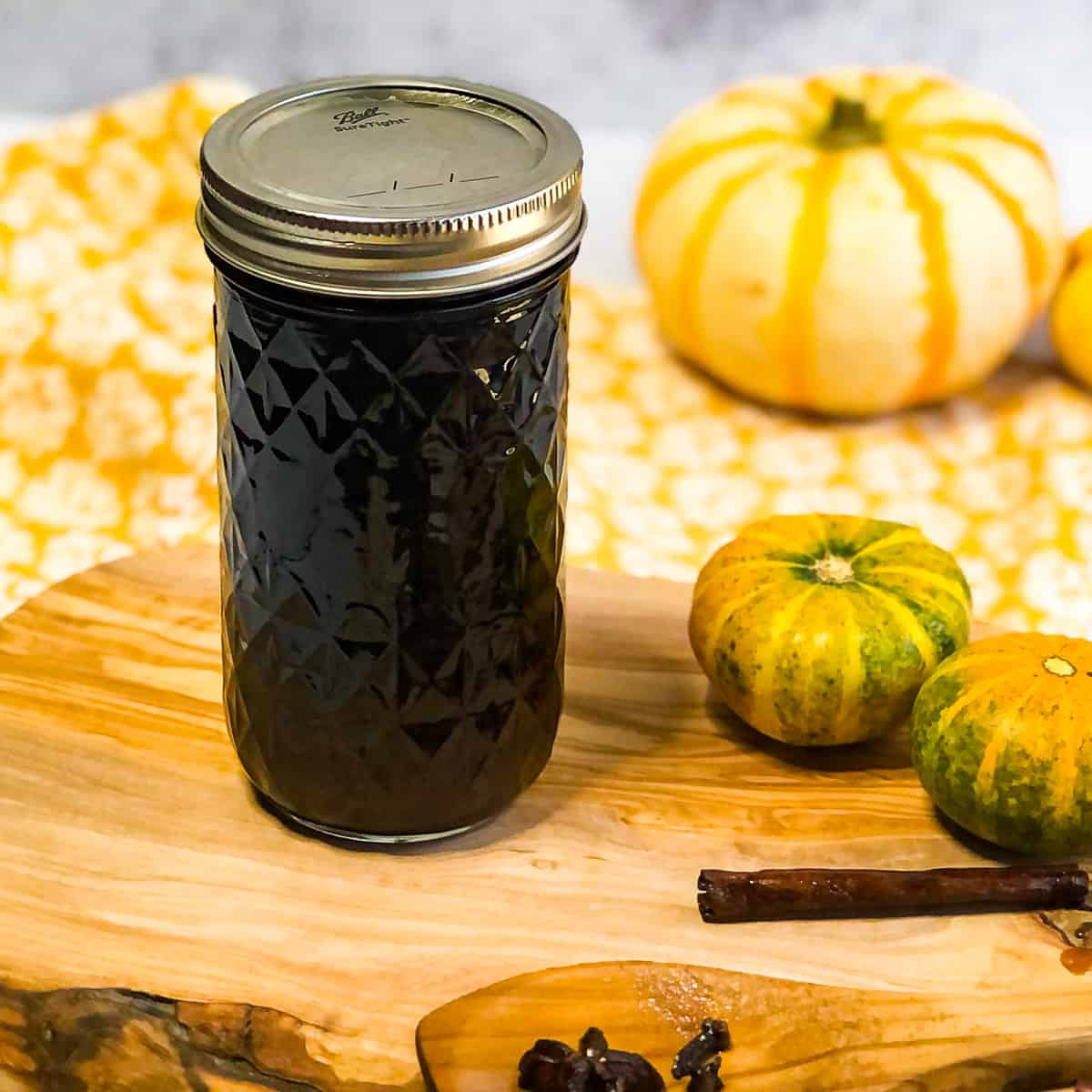 Jar of simple syrup on a wood platter with small pumpkins in background.