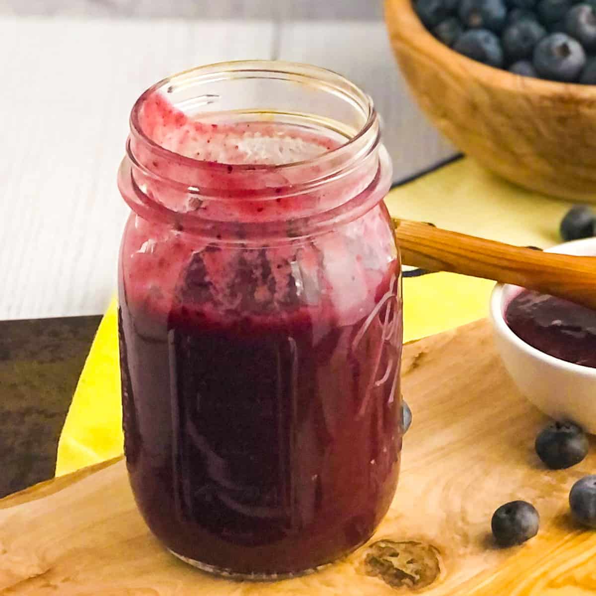 Blueberry sauce in a canning jar with bowl of blueberries in the background.