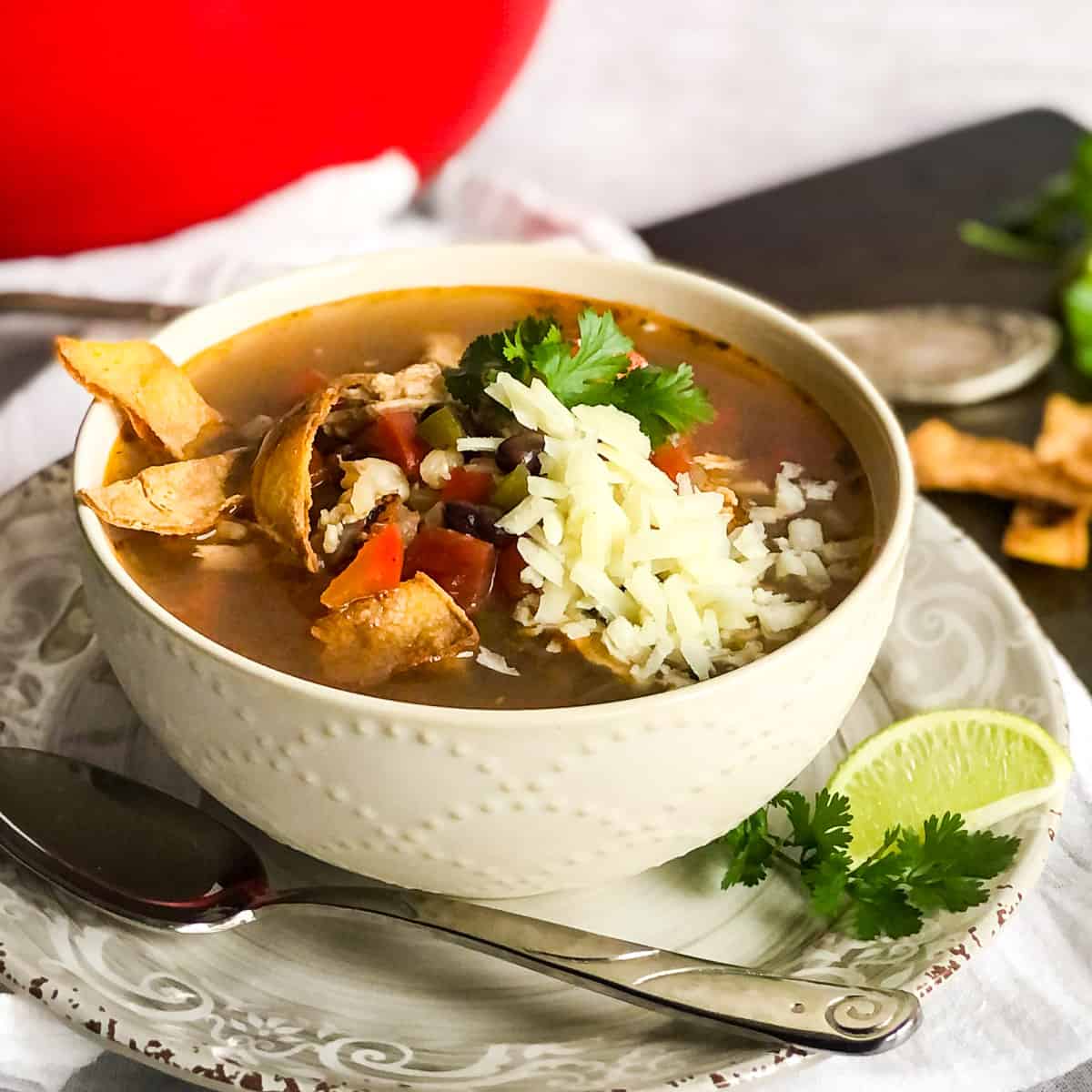 Chicken Tortilla Soup in a white bowl garnished with cheese, cilantro, and tortilla strips.