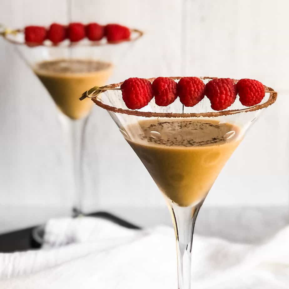 Close up of Chocolate Raspberry Martini garnished with a skewer of raspberries with a second blurred martini in the background.