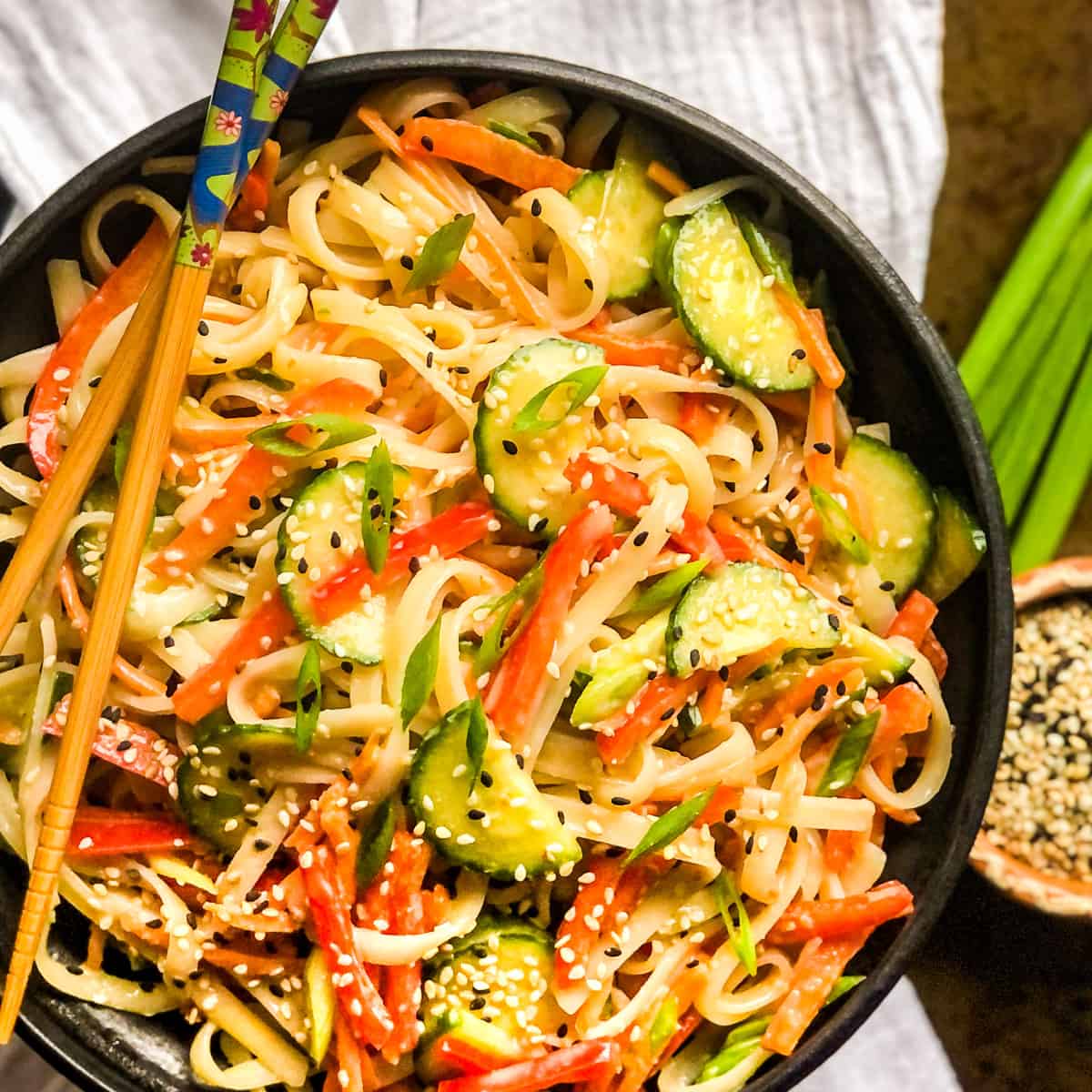 Rice noodle salad in a black bowl with chopsticks resting on top.
