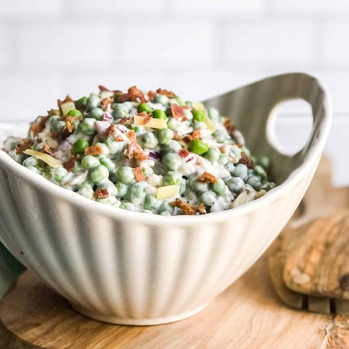 Pea Salad garnished with bacon bits in a white bowl.