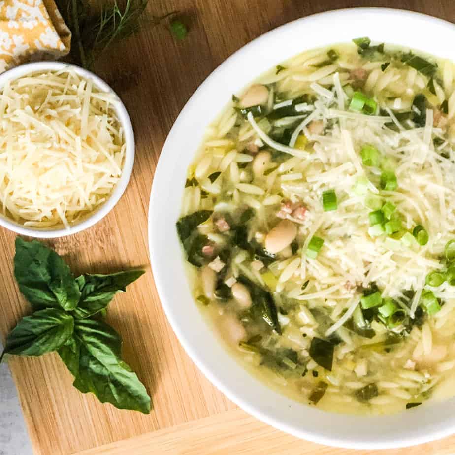 Orzo Soup in a white bowl garnished with shredded parmesan cheese and green onions.