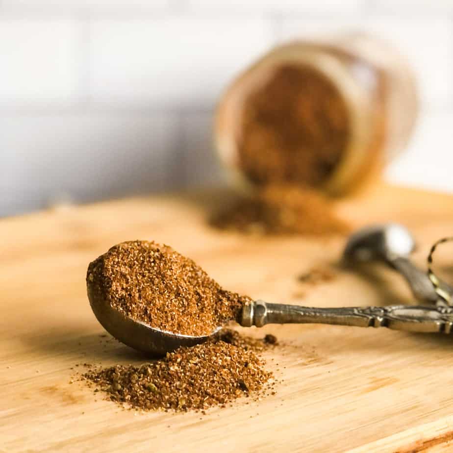 Taco seasoning in a tablespoon on a wood cutting board with bottle of seasoning in background.
