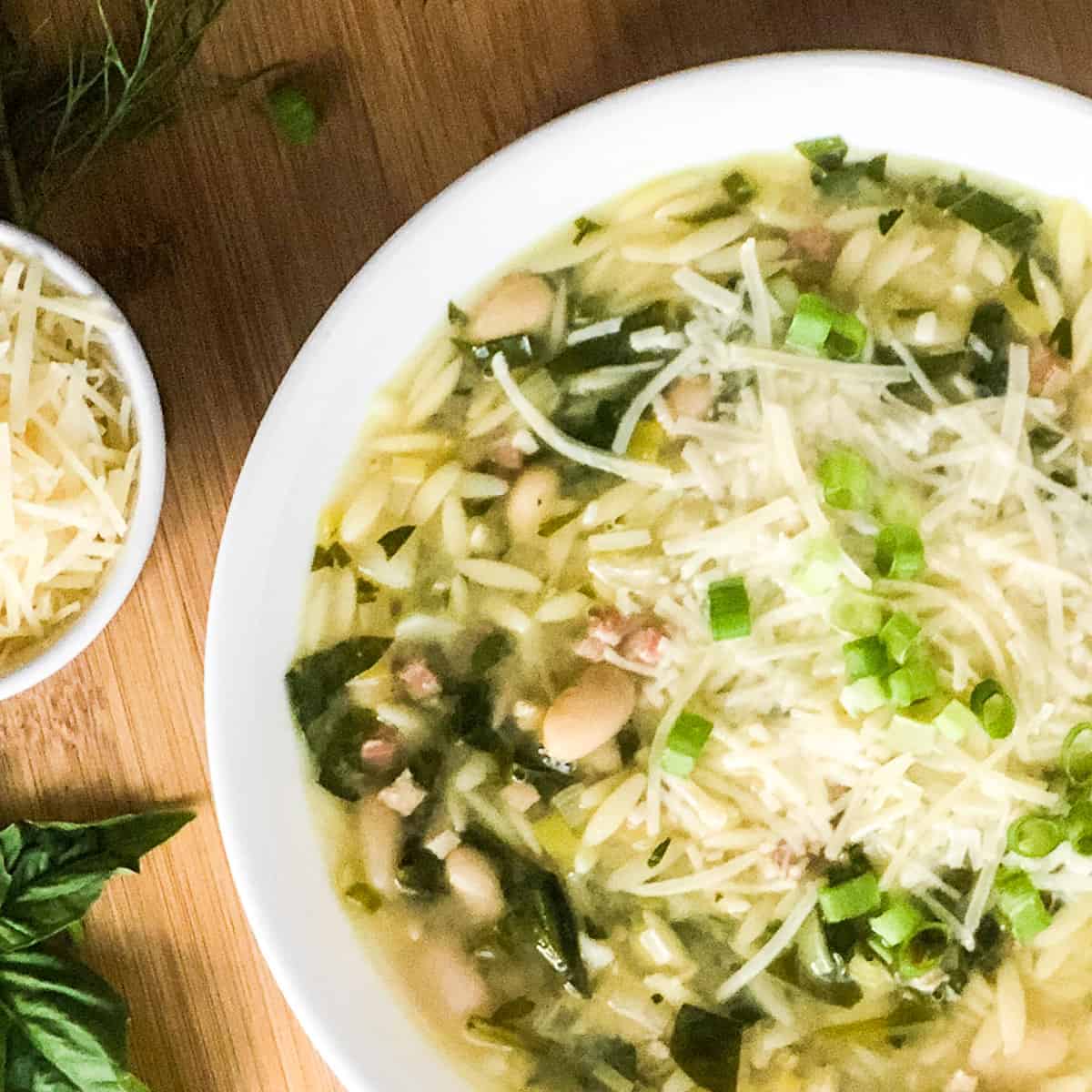 Orzo Soup with basil leaves and bowl of parmesan to the right.