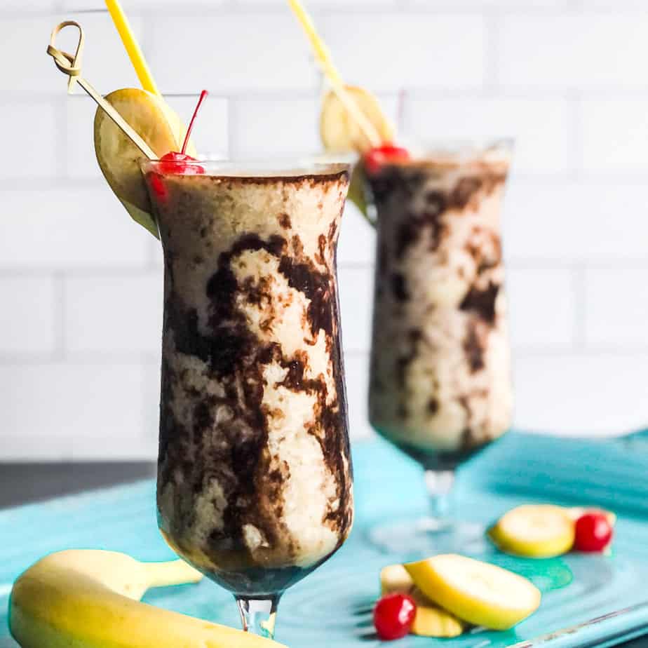 Dirty Banana cocktail in a chocolate drizzled glass garnished with a banana slice and cherry.