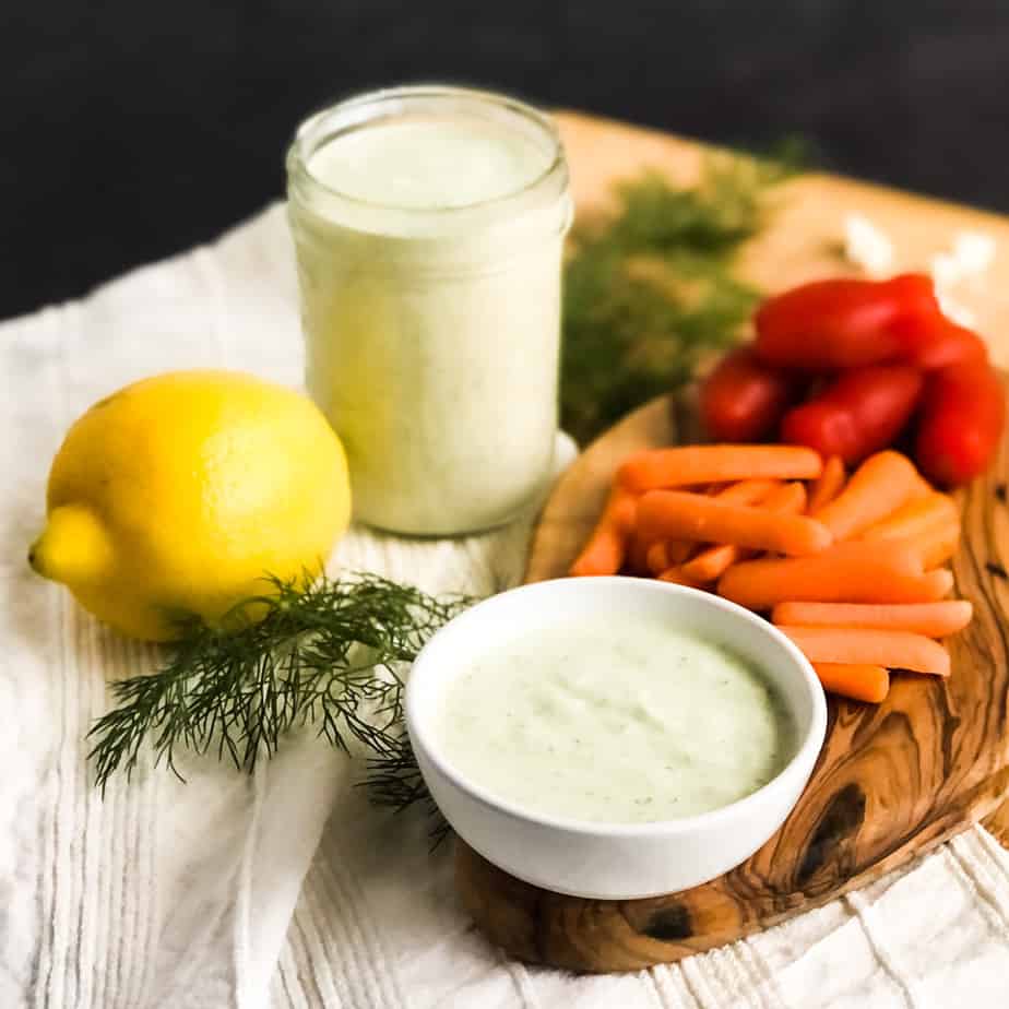 Creamy Greek Feta Dressing in a small bowl on a wood board with carrots and tomatoes in background.