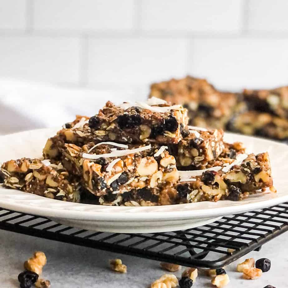 Walnut Bars stacked on a white plate garnished with coconut flakes, walnuts, and dried blueberries.