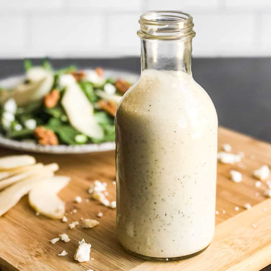 Creamy Gorgonzola Dressing in a glass bottle in front of a salad blurred in background.