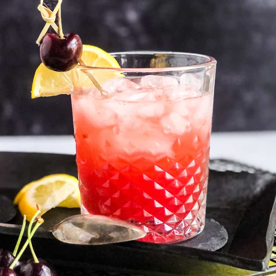 Close up of a single Cherry Bourbon Smash garnished with a lemon wheel and cherry.