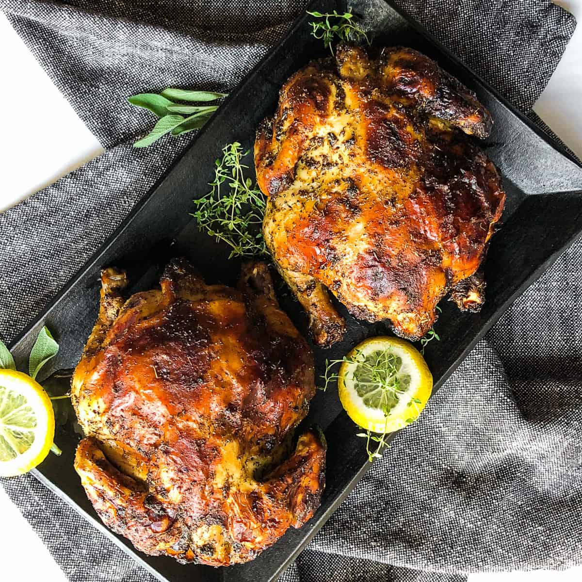 Overhead shot of two Cornish hens on a black platter.