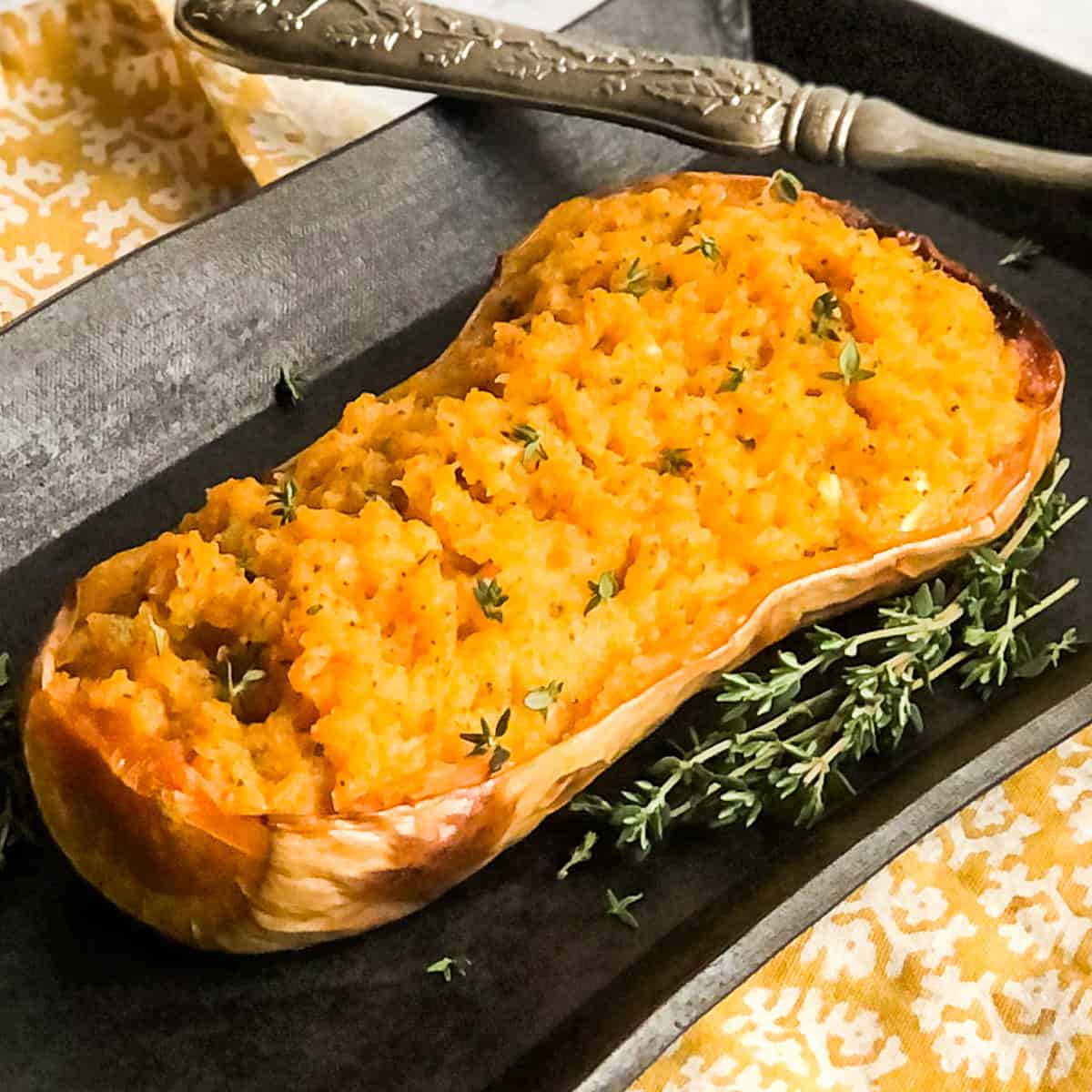 Mashed Butternut Squash inside it's skin on a black platter garnished with fresh thyme springs.