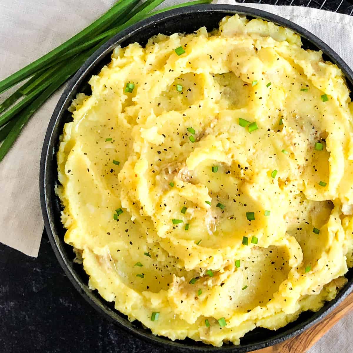 Overhead shot of Parsnip Mashed Potatoes in a black bowl garnished with fresh chives.
