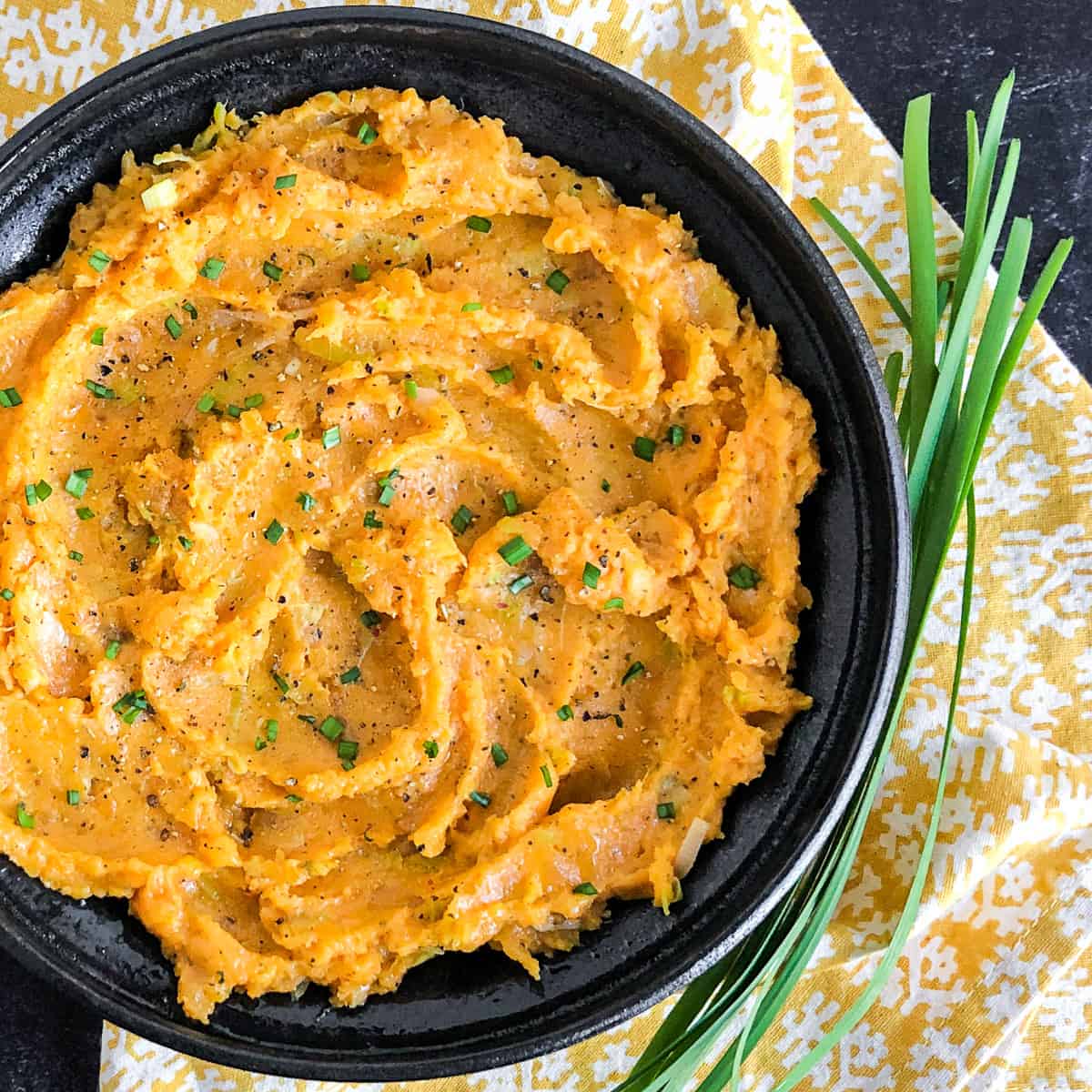 Savory Sweet Potato Mash in a black bowl garnished with fresh chives.