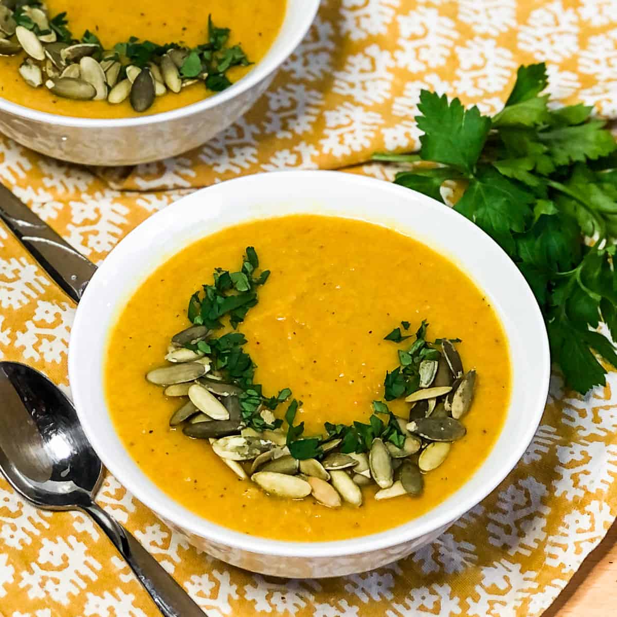Butternut Squash Soup in a white bowl garnished with pepitas and chopped herbs.