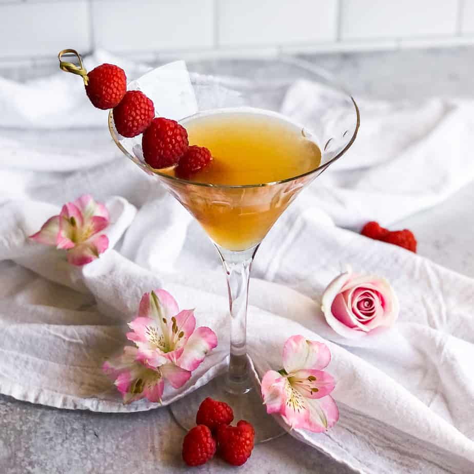 Close up of French Martini surrounded by pink flowers and garnished with raspberries.