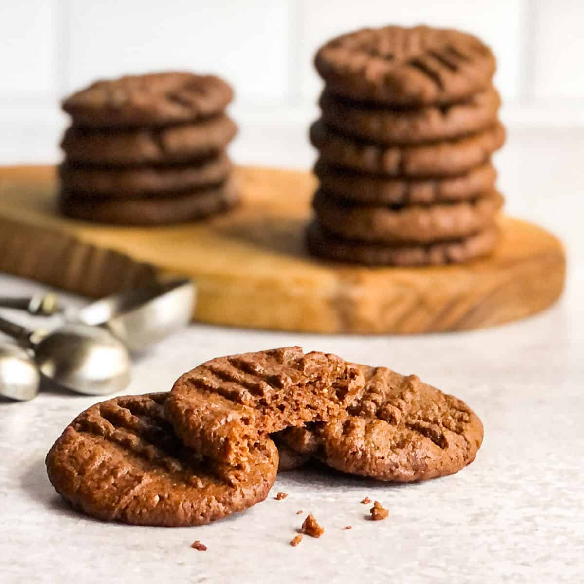 Three almond butter cookies with stacks of cookies in background.