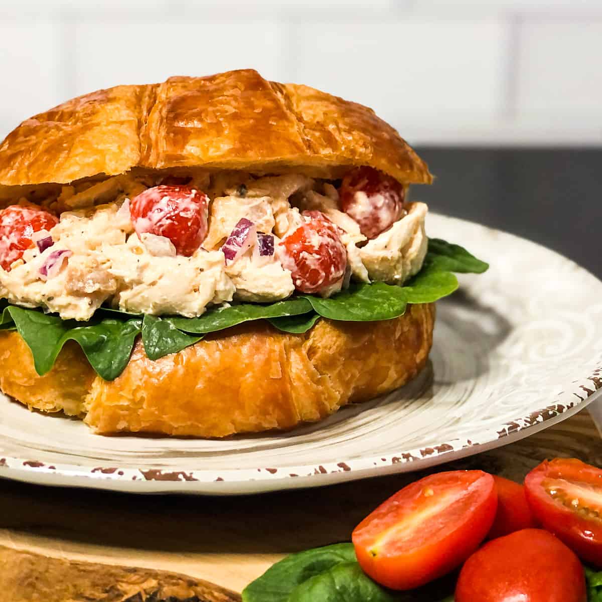 BLT Chicken Salad in a croissant with spinach on a neutral plate.