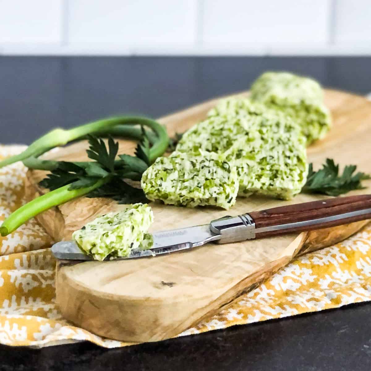 Garlic Scape Butter slice on a knife with additional slices in background.